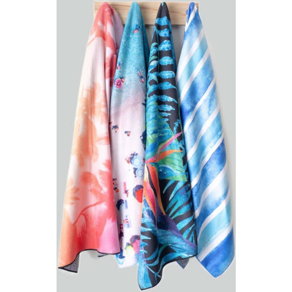 A set of medium sand-free towels in vibrant colours, featuring floral and abstract patterns, hanging on a display.