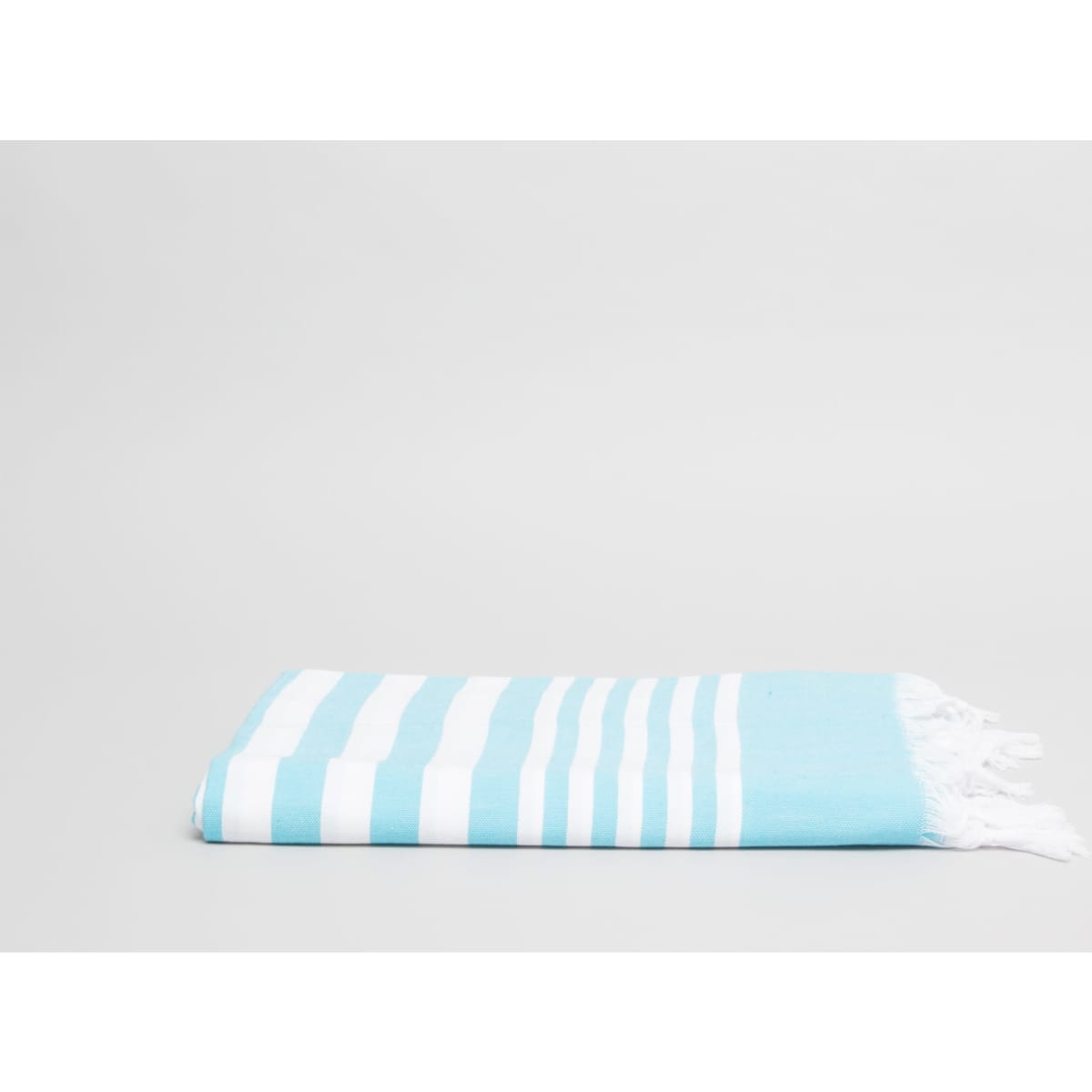 A folded Turkish beach and pool towel in aqua blue with white stripes and tasselled edges.
