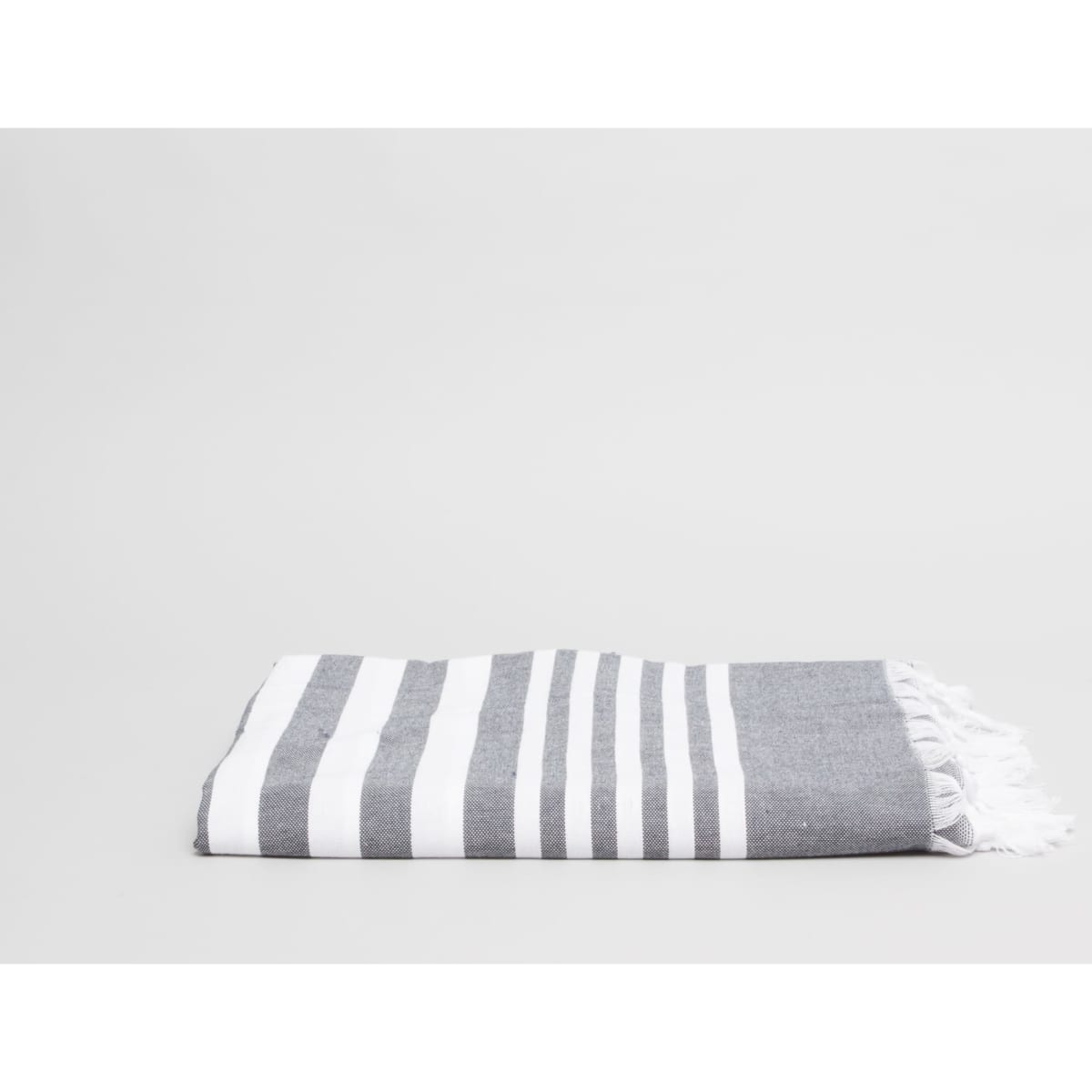 A folded charcoal grey beach and pool towel with white stripes and fringed edges.