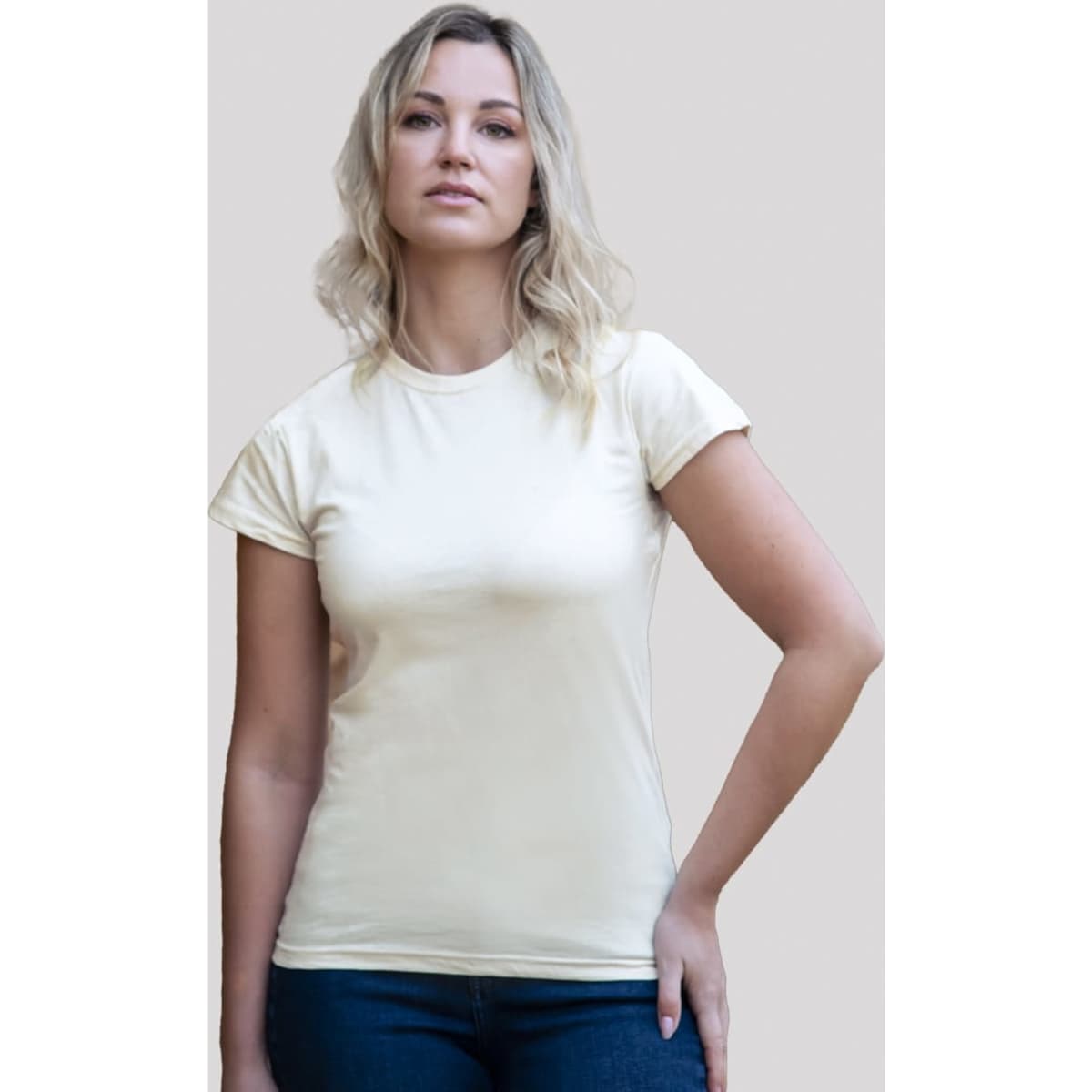 A woman wearing a light yellow organic T-shirt, standing against a plain background. The shirt has a logo.