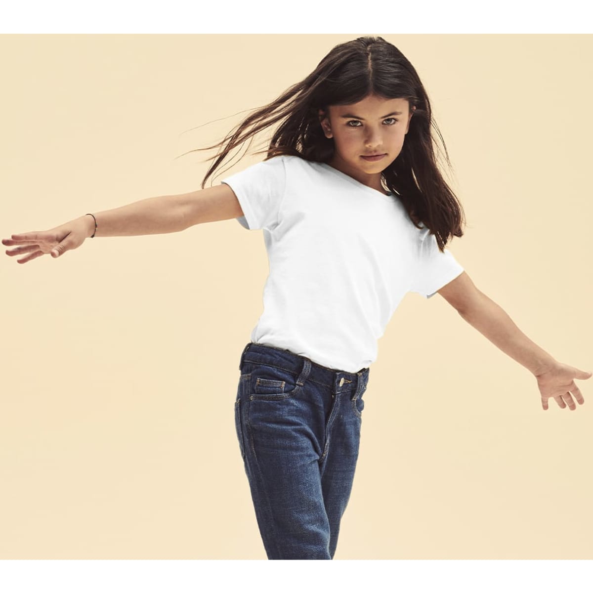A girl models a white t-shirt paired with blue jeans, displaying a confident pose against a neutral background.