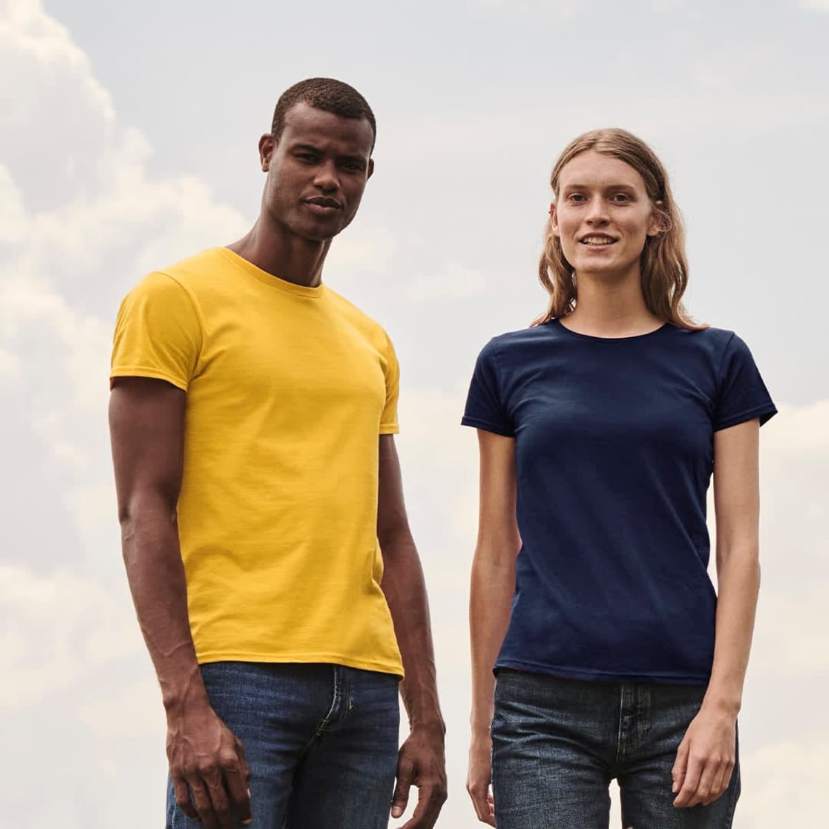 A yellow t-shirt on a man and a navy t-shirt on a woman, both standing outdoors against a cloudy sky.