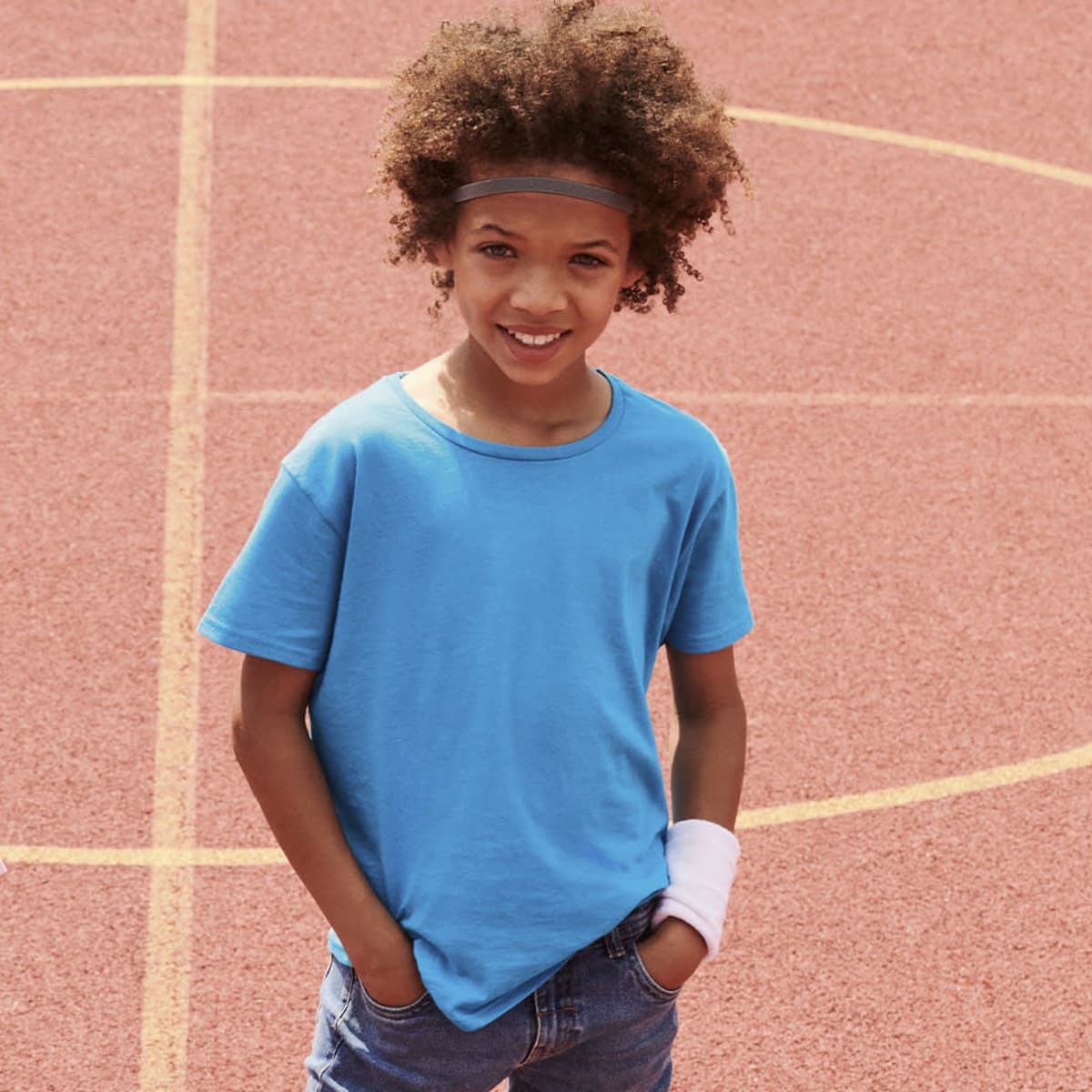 A blue t-shirt worn by a child with curly hair, standing on a sports court with a friendly smile.