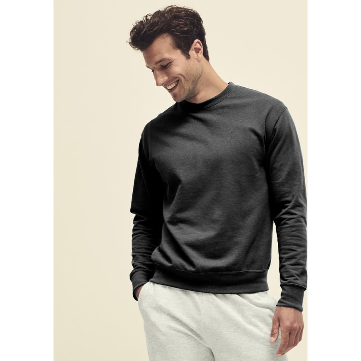 A man wearing a black lightweight set-in hoodie, paired with light grey pants, smiling while looking down.