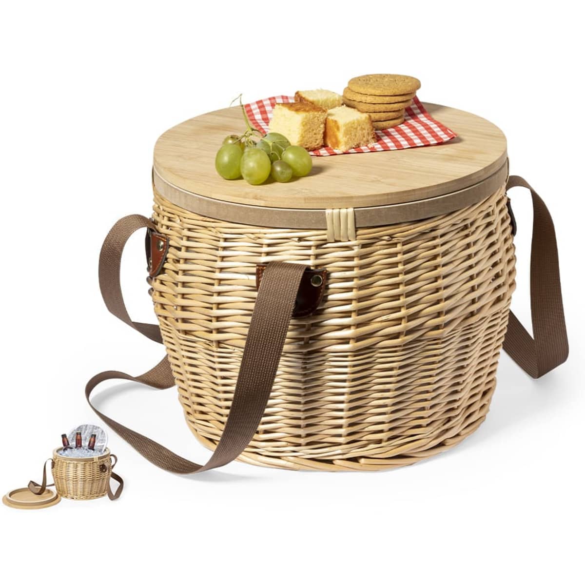 A woven picnic cooler in natural tones with a wooden lid, featuring grapes, cake, and biscuits on top. Brown straps included.