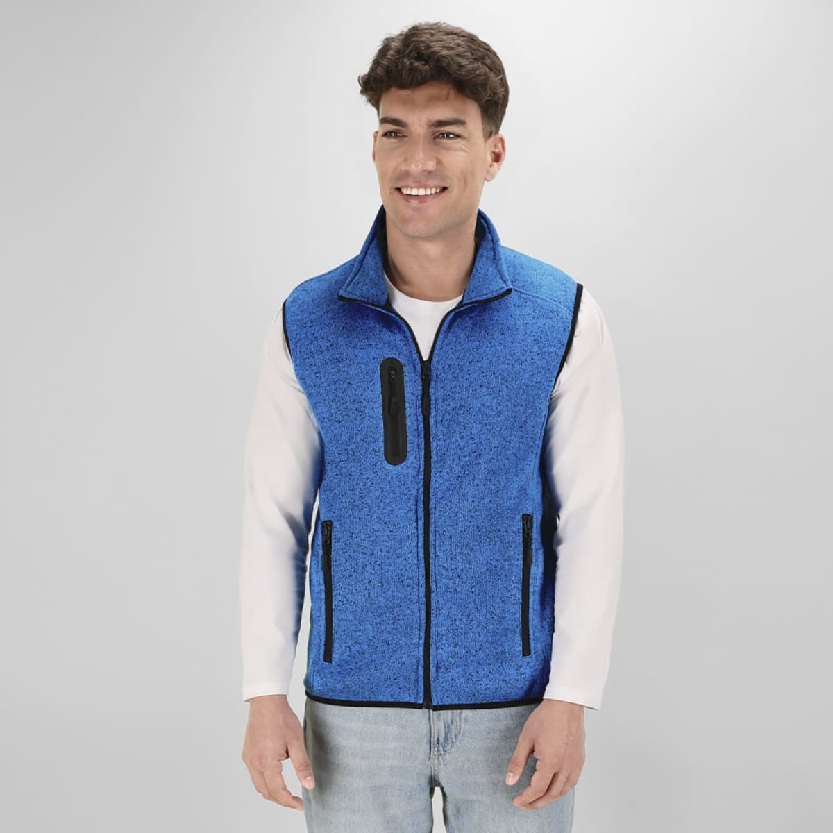 A blue textured vest is worn by a smiling person, featuring zippers and a logo on the front.