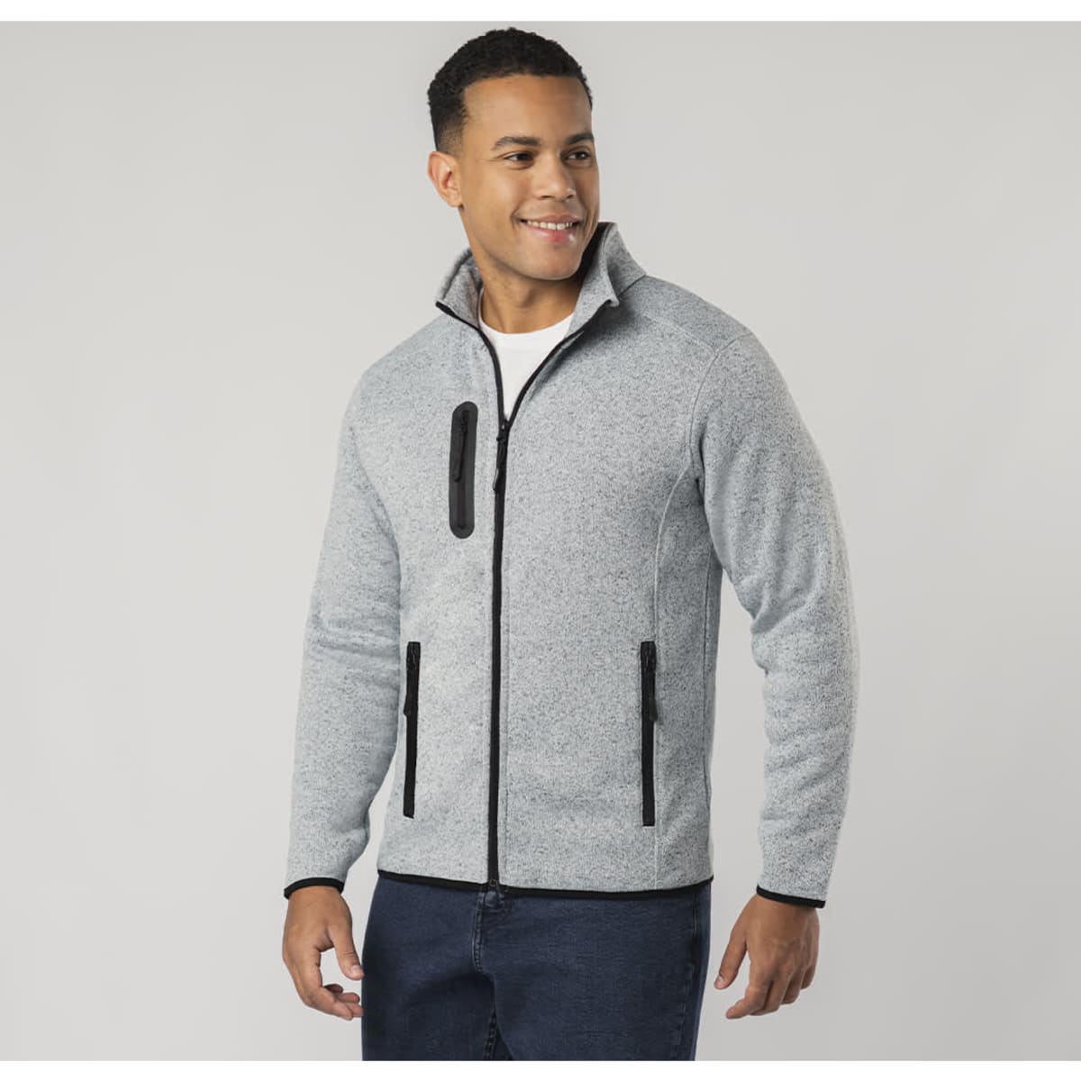 A man wearing a grey polar fleece jacket with black zippers and a collar, smiling at the camera.