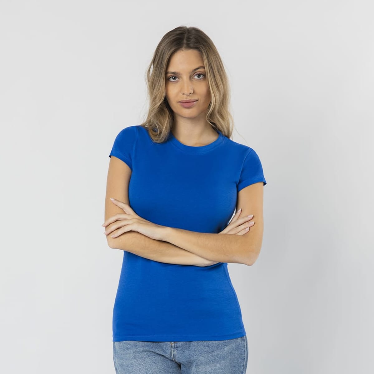 A fitted blue T-shirt on a model with long hair, standing with arms crossed against a plain background.