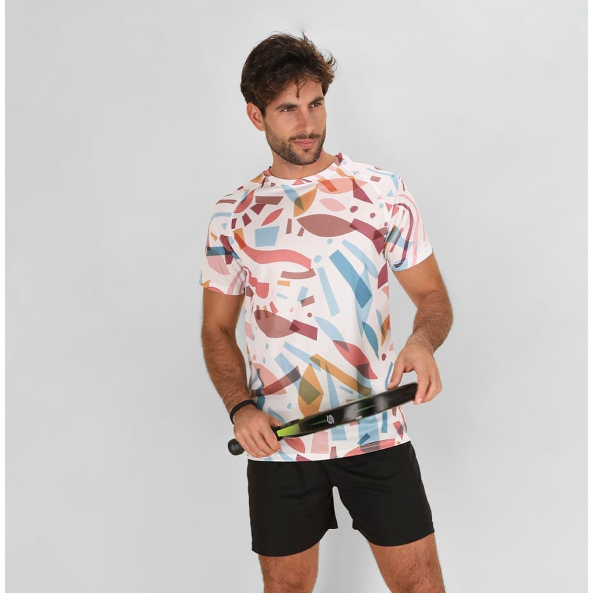 A casual t-shirt featuring a multicoloured abstract pattern, worn by a man holding a tennis racquet.