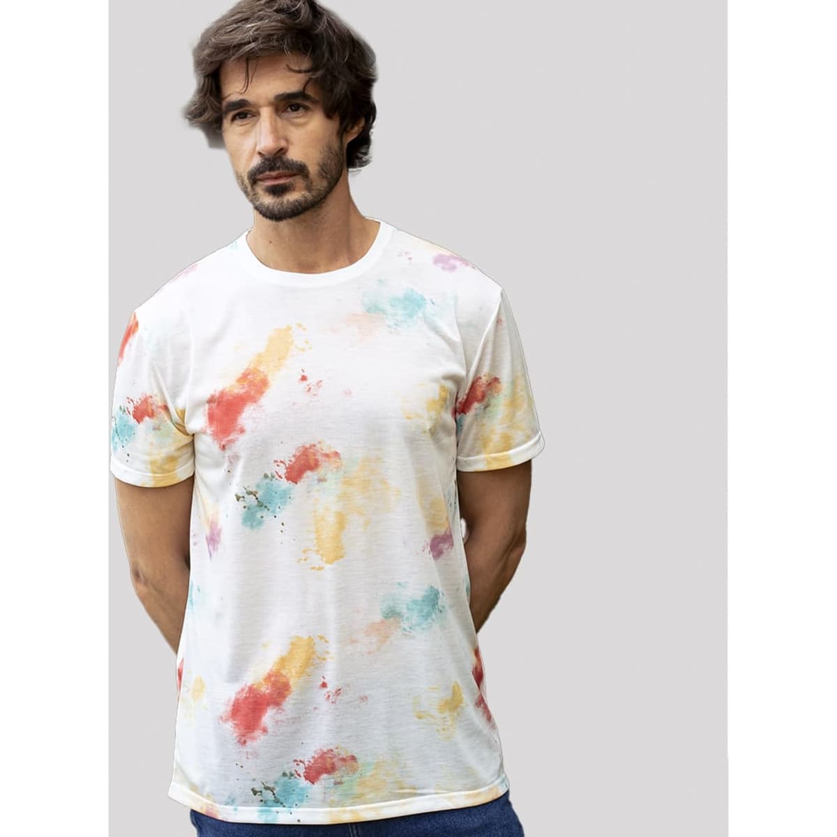 A man wearing a white t-shirt with a multicoloured splash pattern in red, yellow, and teal. The shirt has a logo.