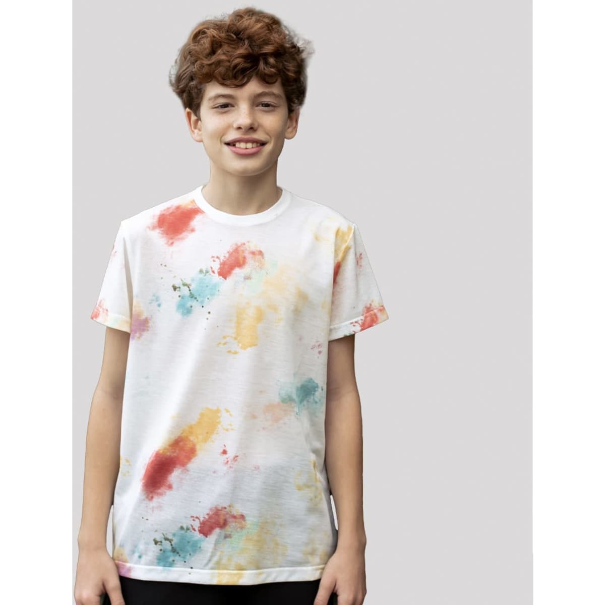 A child is wearing a white T-shirt featuring a vibrant, multi-colour splash design in red, blue, and yellow.