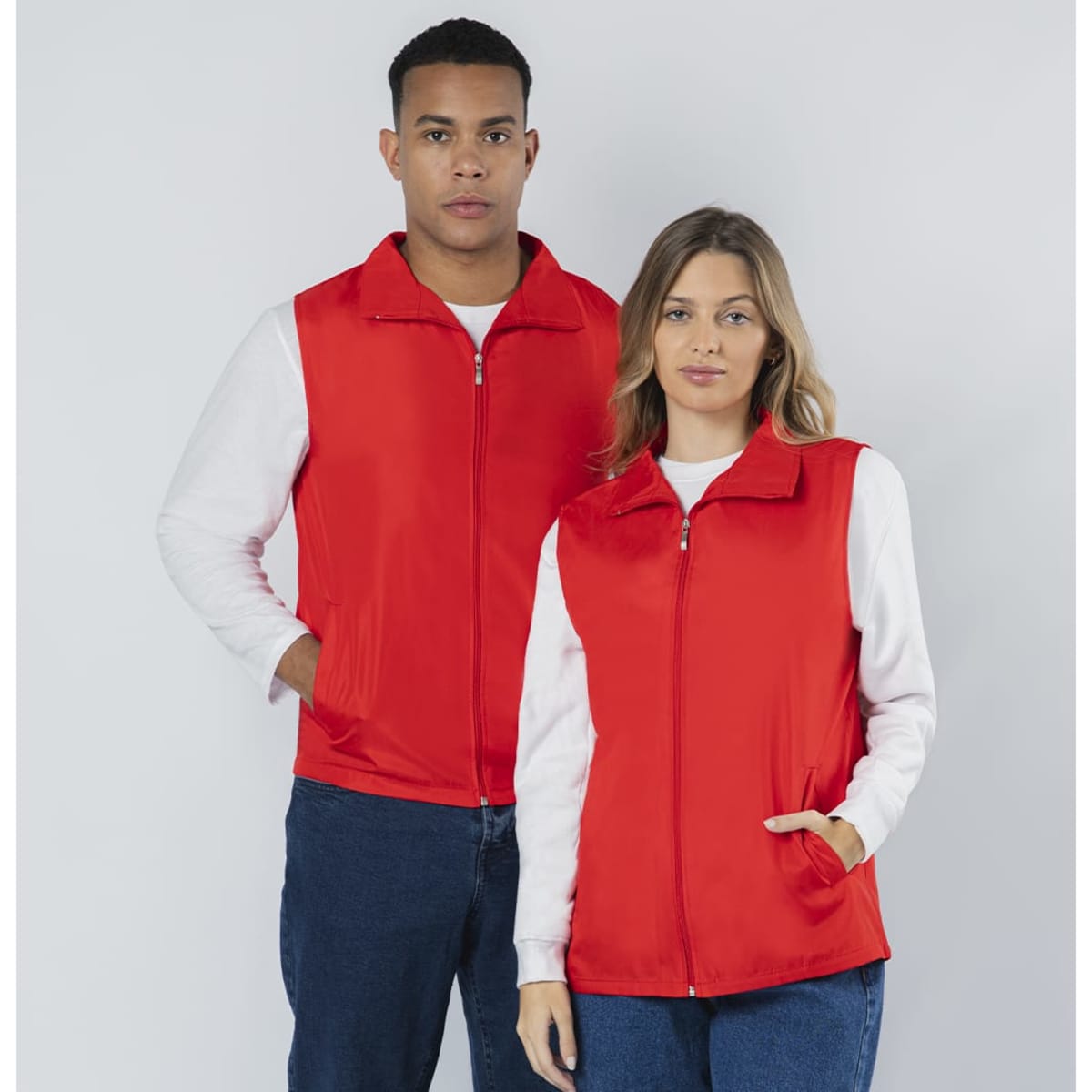 A red vest jacket featuring a zip closure and side pockets, modelled by a man and a woman. The jacket has a logo.