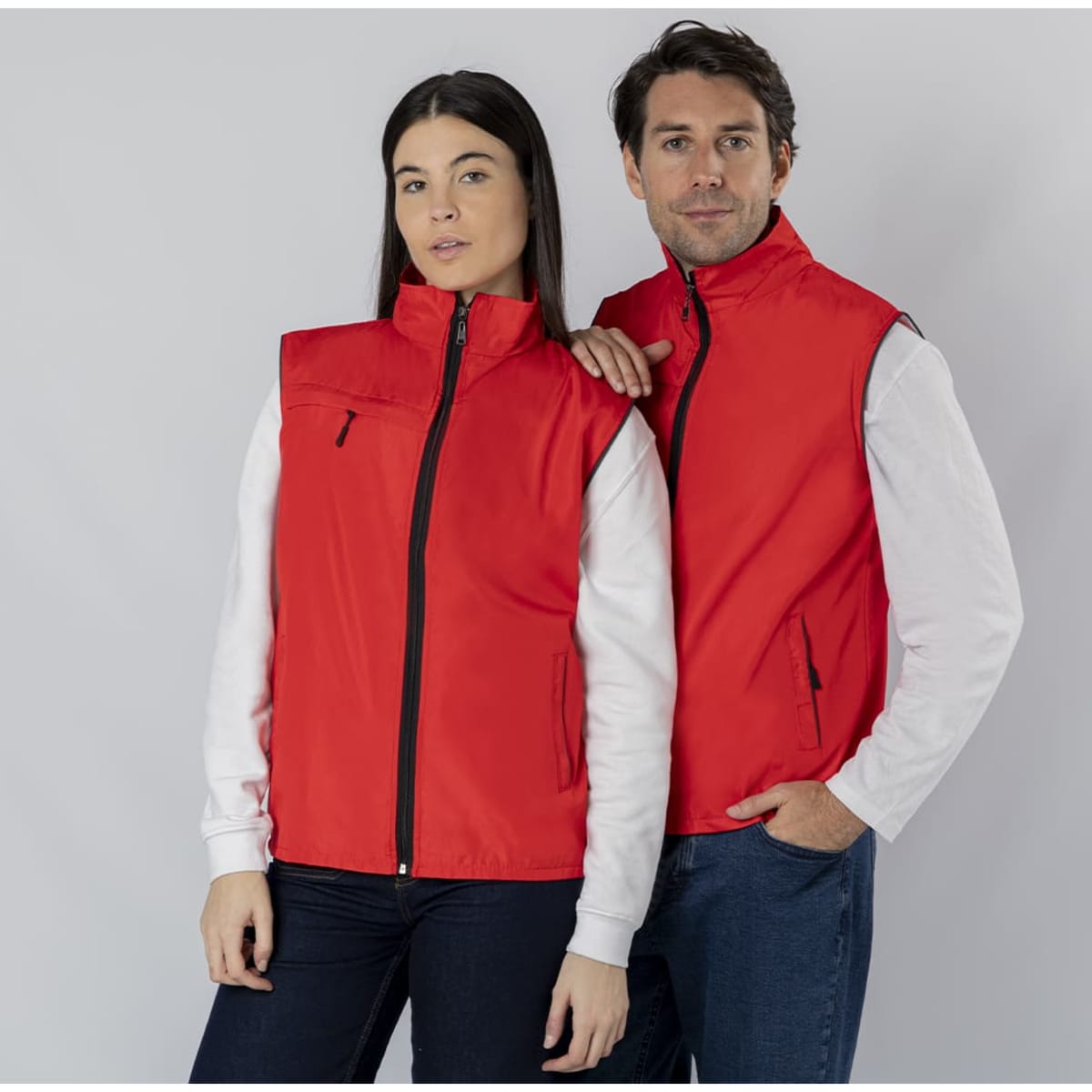 A red vest jacket is worn by a man and a woman, featuring a zip closure and a front pocket.