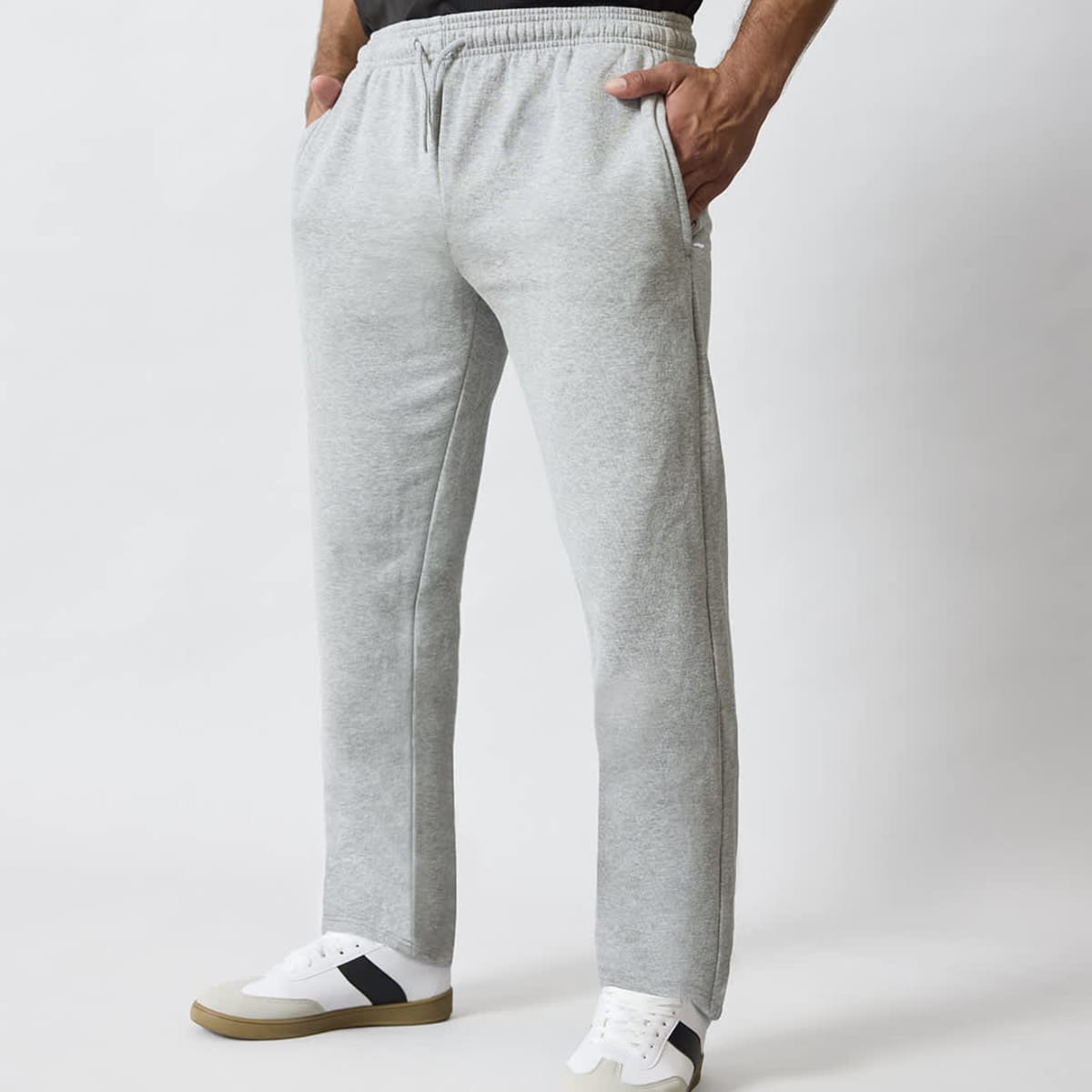 A pair of grey track pants with side pockets, featuring an elastic waistband, modelled with white shoes.