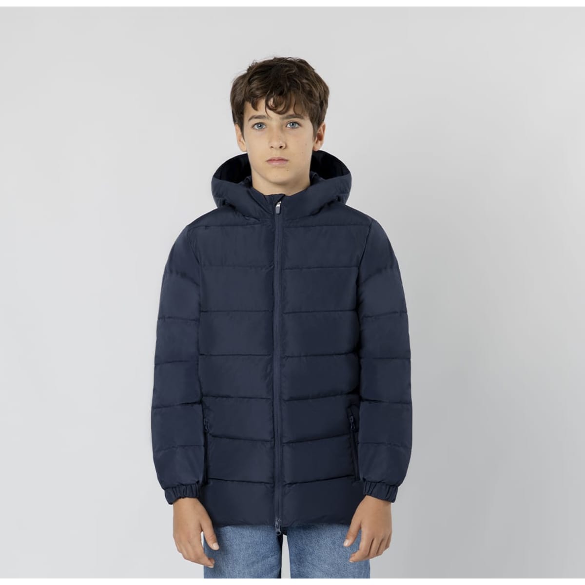 A puffer jacket in navy blue worn by a young model with a hood. The jacket features a zip and elastic cuffs.