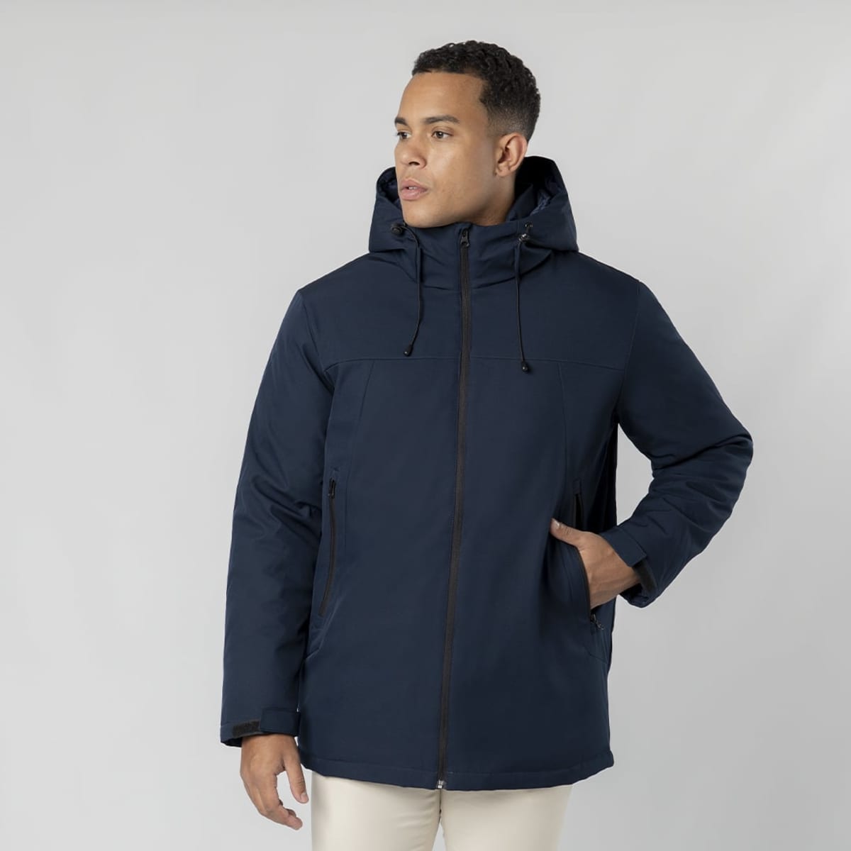A puffer jacket in navy blue, featuring a hood and zip closure. The model is standing with one hand in a pocket.