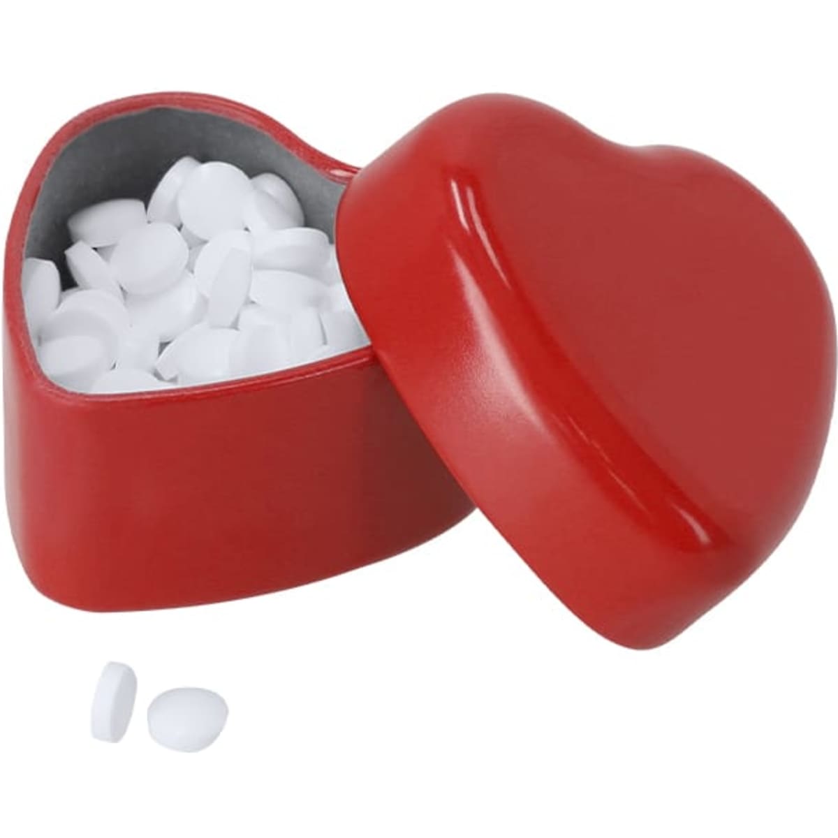 A red heart-shaped container filled with white mints, with a few mints scattered beside it.