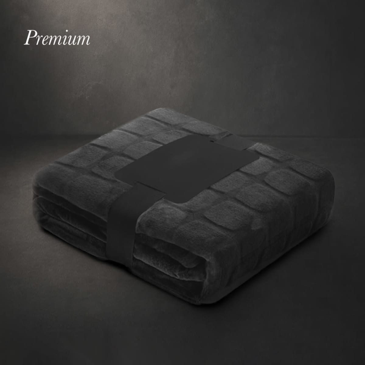 A dark grey blanket is neatly folded and secured with a black band, featuring a logo.