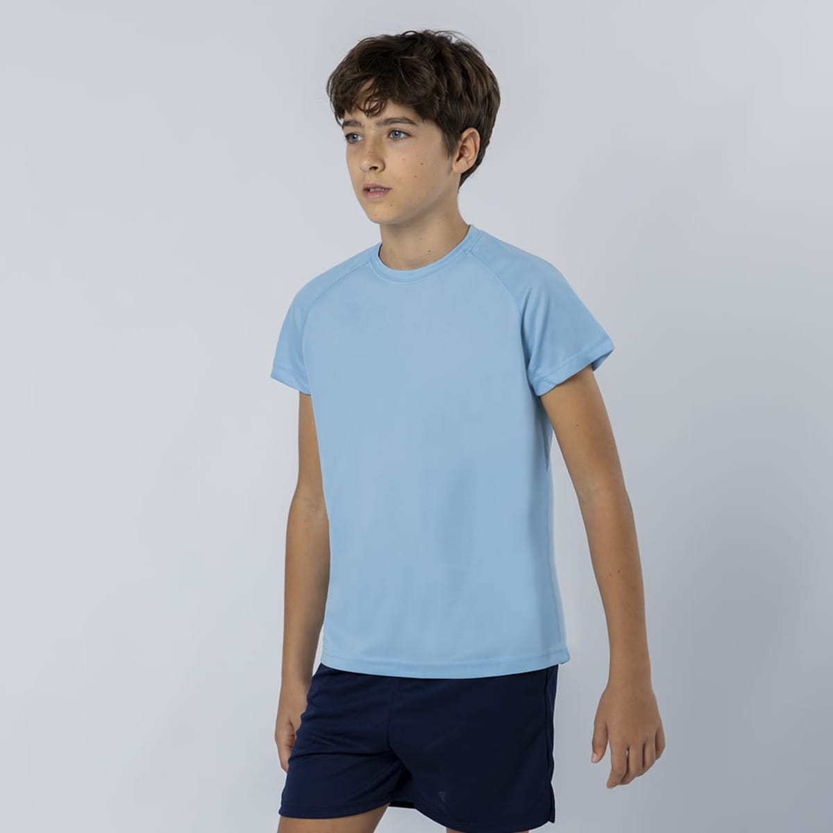 A light blue T-shirt with short sleeves displayed on a young model wearing navy shorts, featuring a logo.