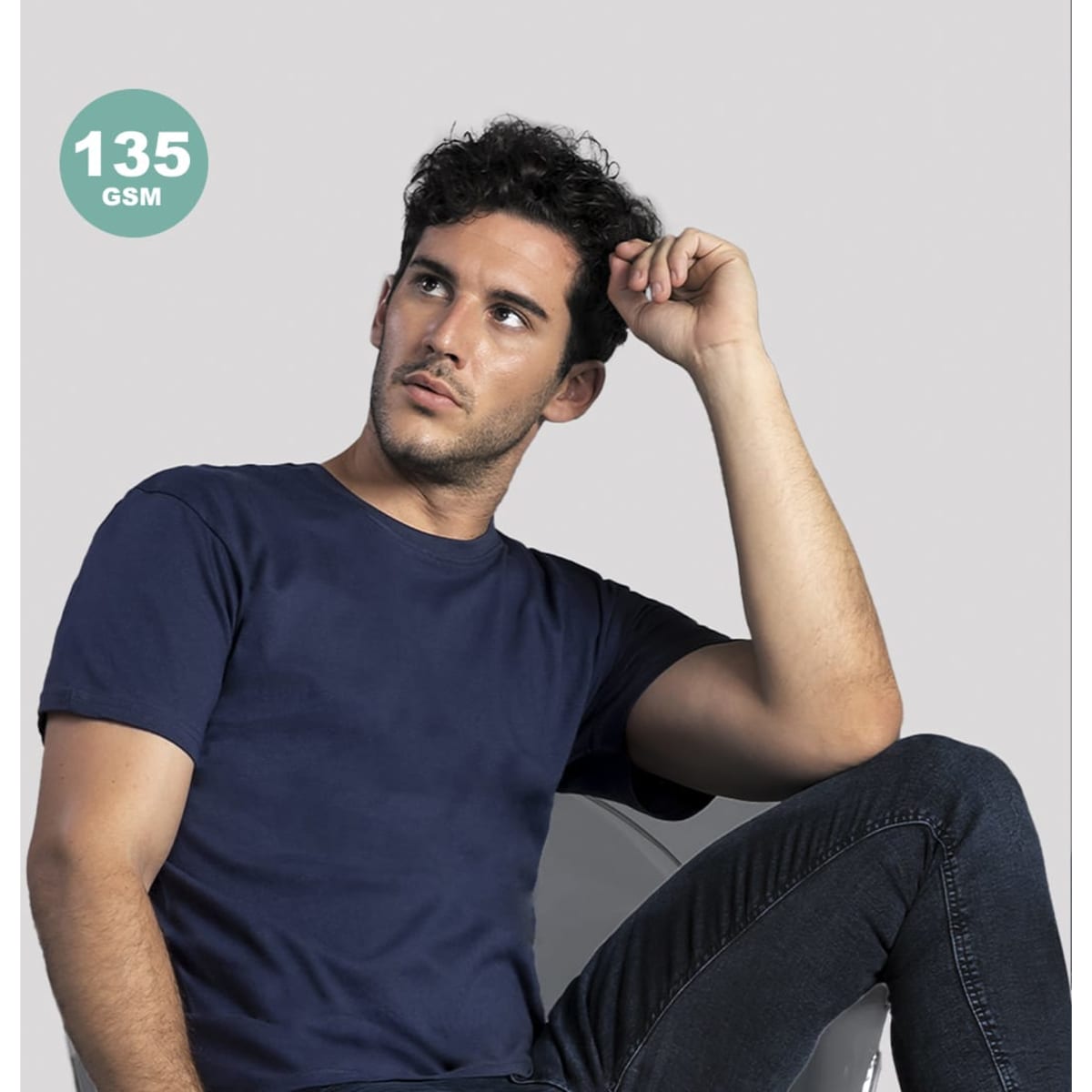 A navy adult colour t-shirt displayed on a seated model, featuring a logo in the corner. Model is wearing jeans.