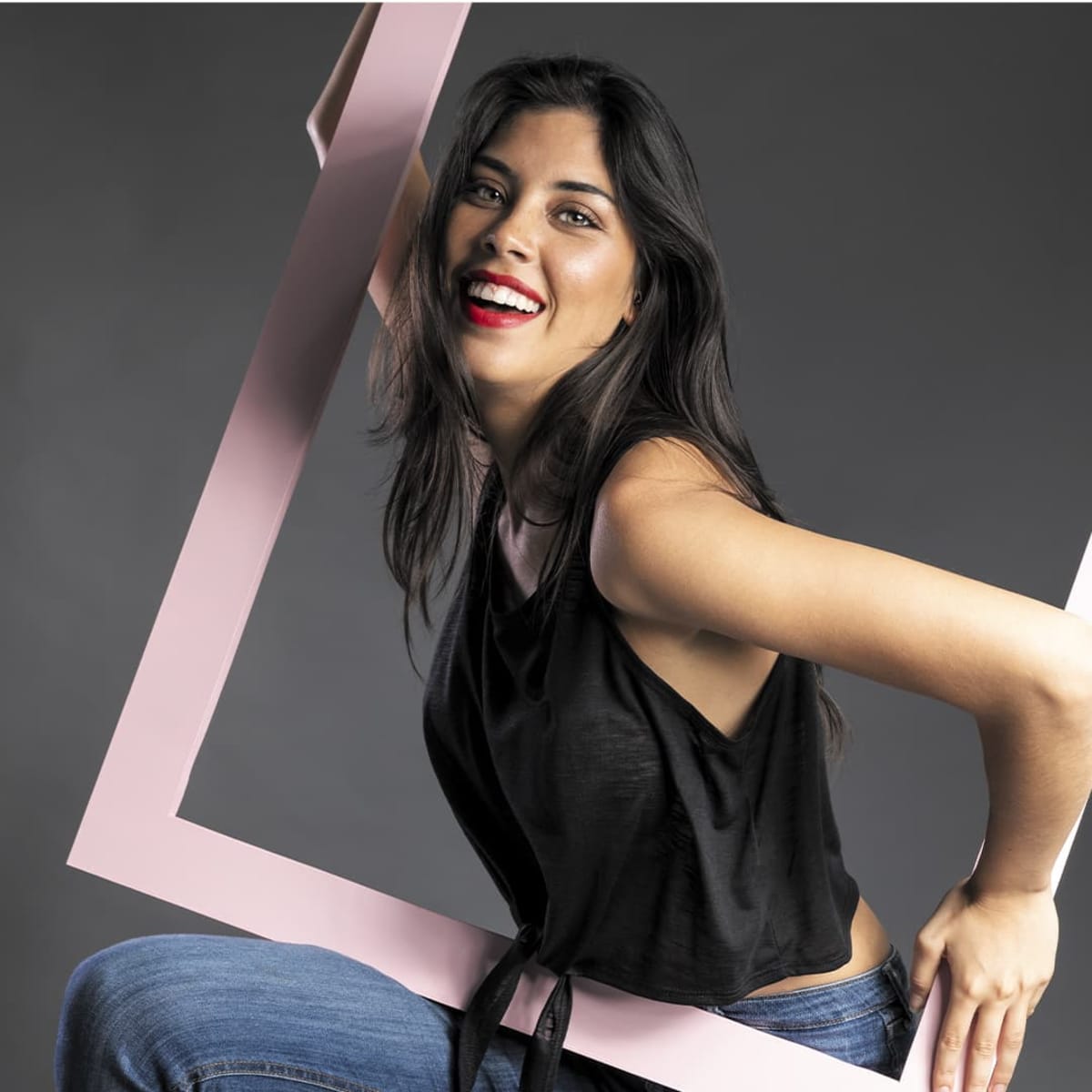 A model wearing a black Slem T-Shirt, posing playfully with a large pink frame and smiling.