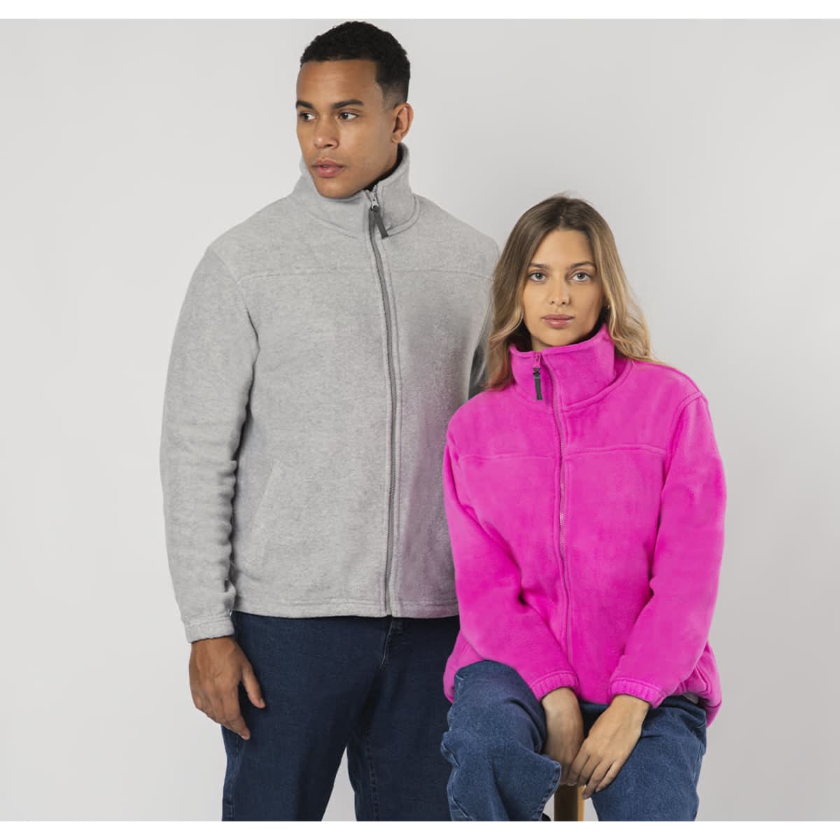 A polar fleece jacket in grey worn by a man and a bright pink version worn by a woman, both featuring a logo.