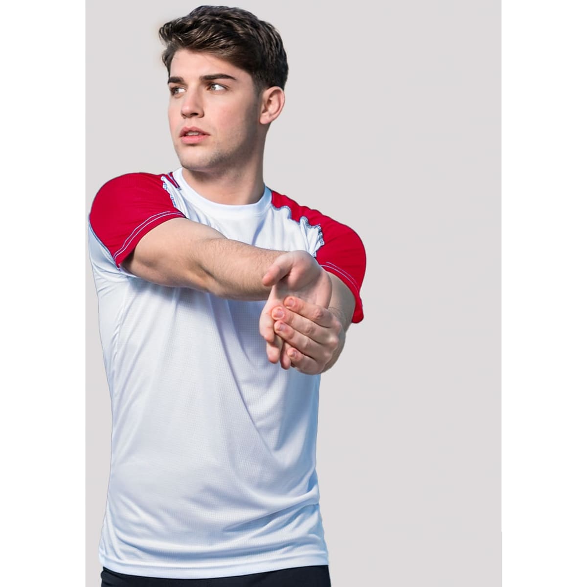 A fitted white T-shirt with red sleeves, featuring a logo, worn by a young man stretching his arms.