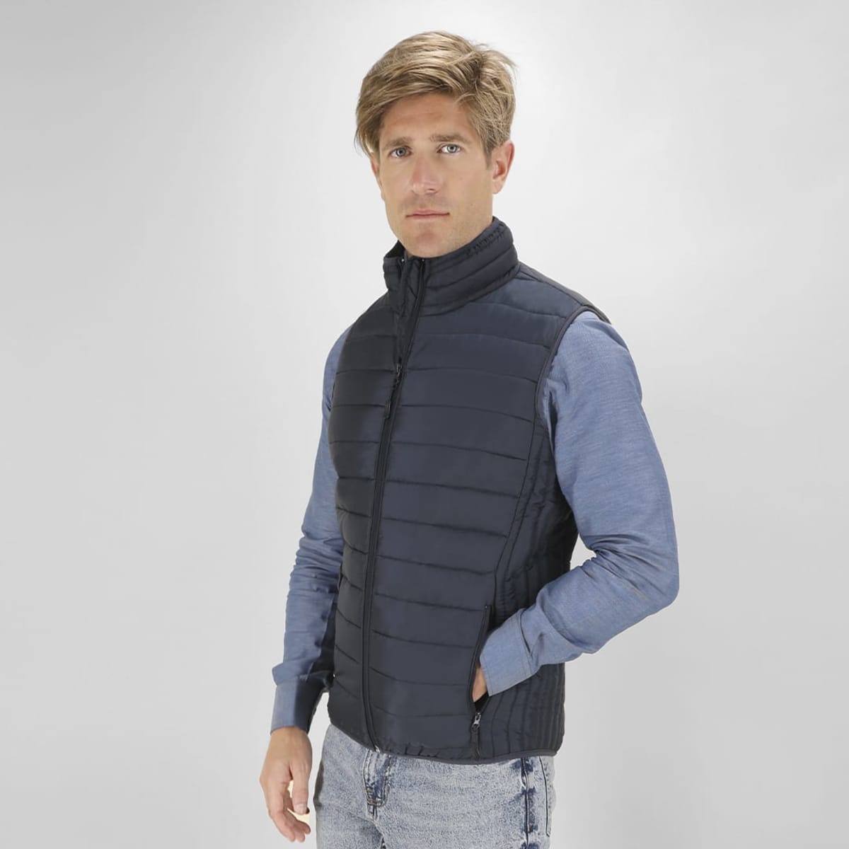 A man wears a navy puffer vest, featuring a zip front and high collar, paired with a blue long-sleeve top.