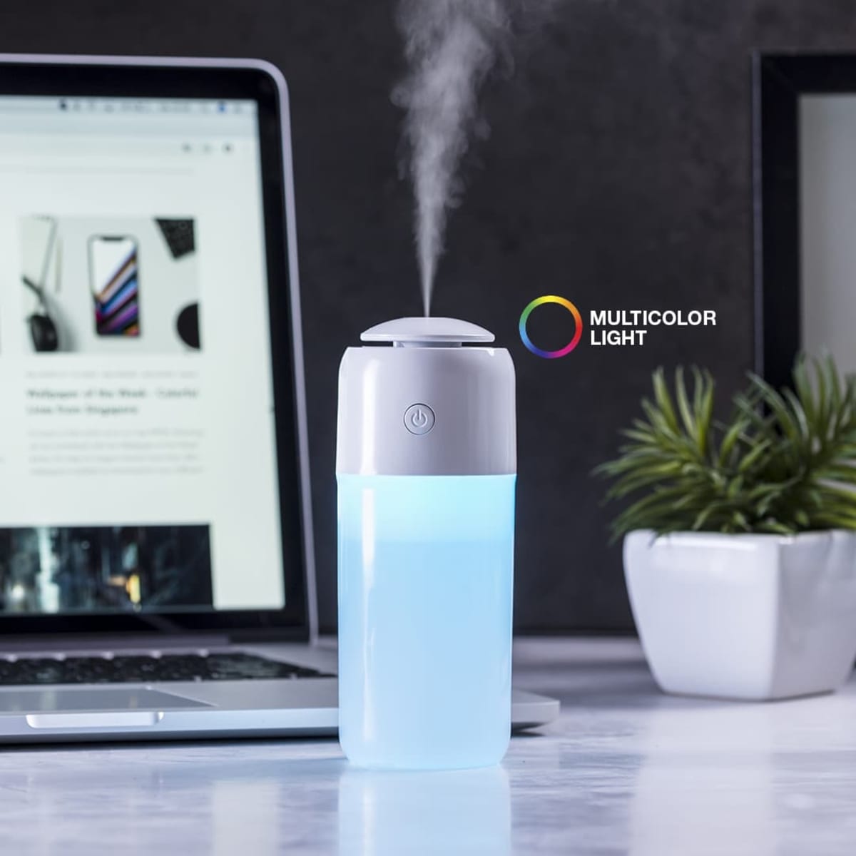 A white and blue humidifier with a multicoloured light feature sits beside a laptop on a desk.