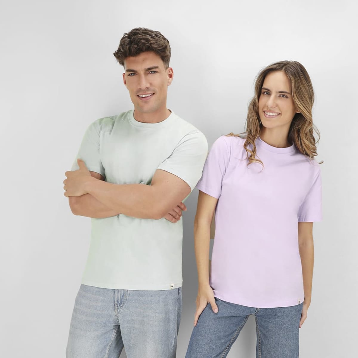 Two models wearing T-shirts; one in mint green and the other in light purple. Both shirts have logos.