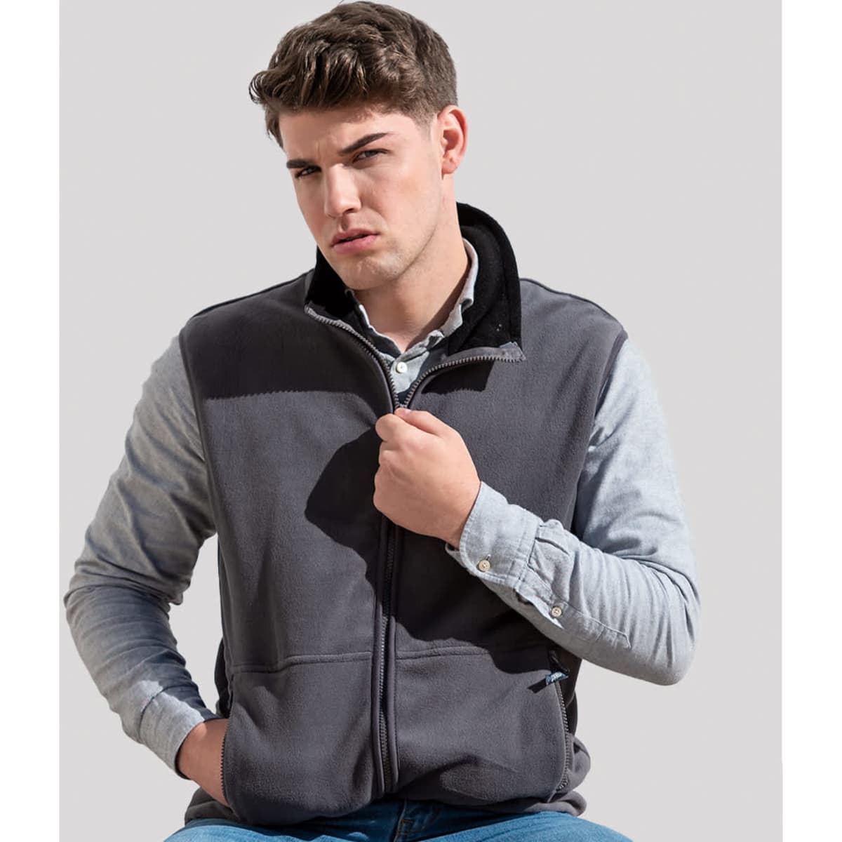 A man wearing a grey polar fleece jacket with a zip, featuring a black collar and logo.