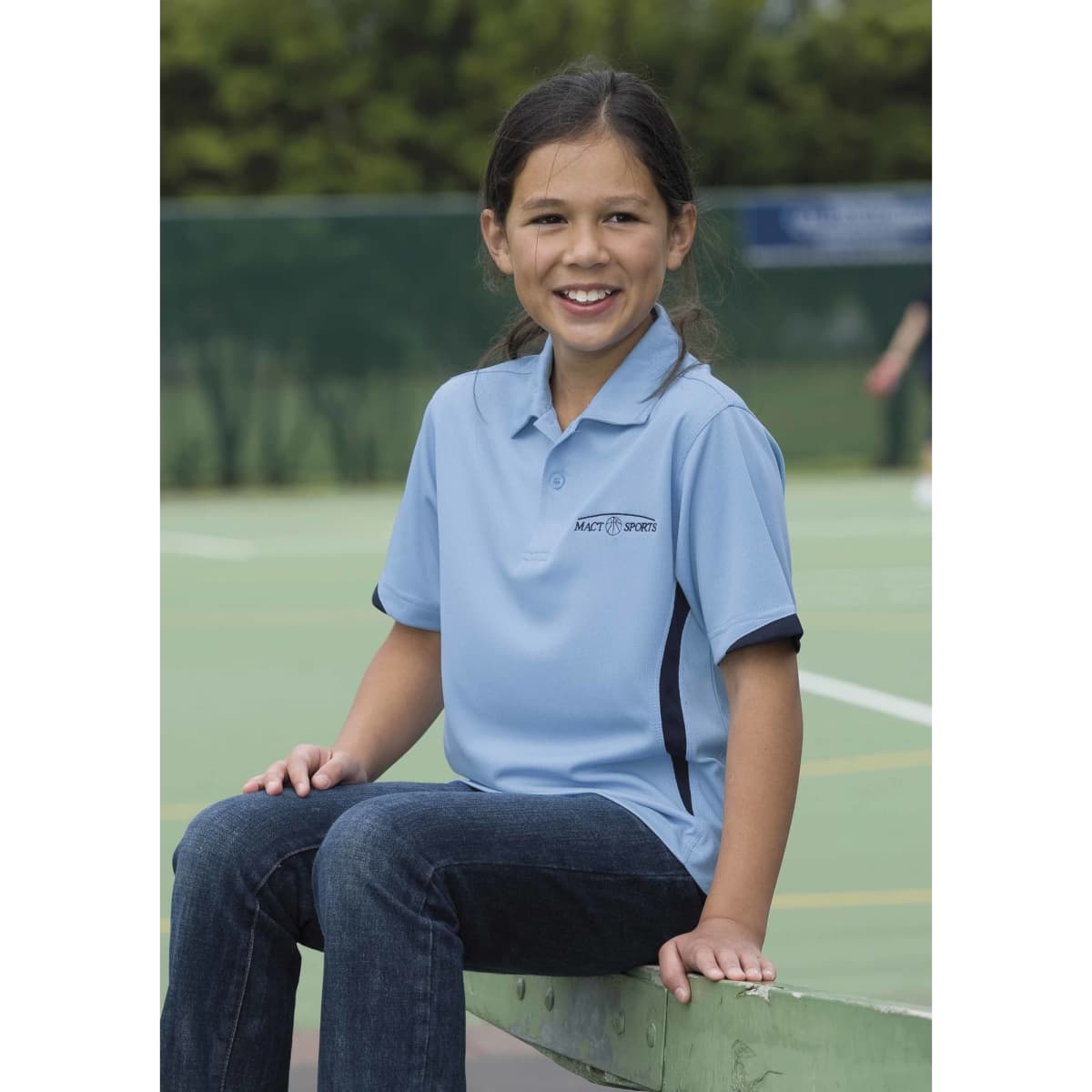 A light blue polo shirt with dark accents, featuring a logo, worn by a smiling girl seated on a court.