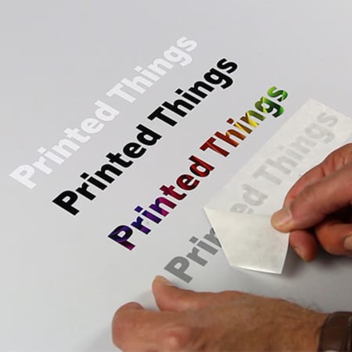 Transfer stickers in various colours, with a person's hand peeling one off a backing sheet. The background is white.