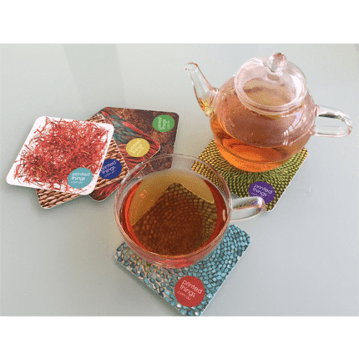 A tea pot and a cup filled with tea, resting on colourful semi-rigid card coasters with a textured design.