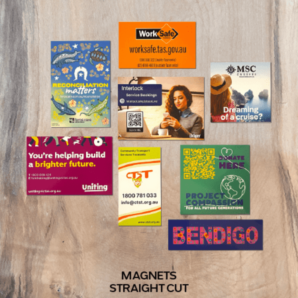 A variety of colourful fridge magnets displayed on a wooden surface, featuring different designs and logos.