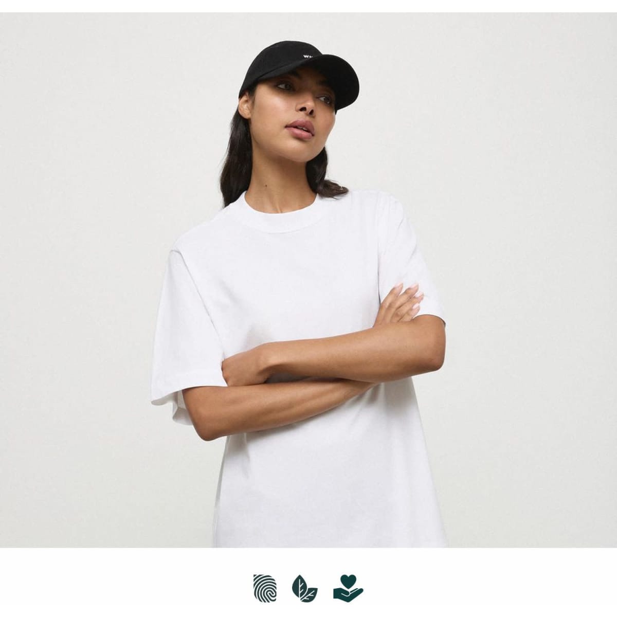 A white t-shirt displayed on a person wearing a black cap. The shirt has a relaxed fit and includes branding.