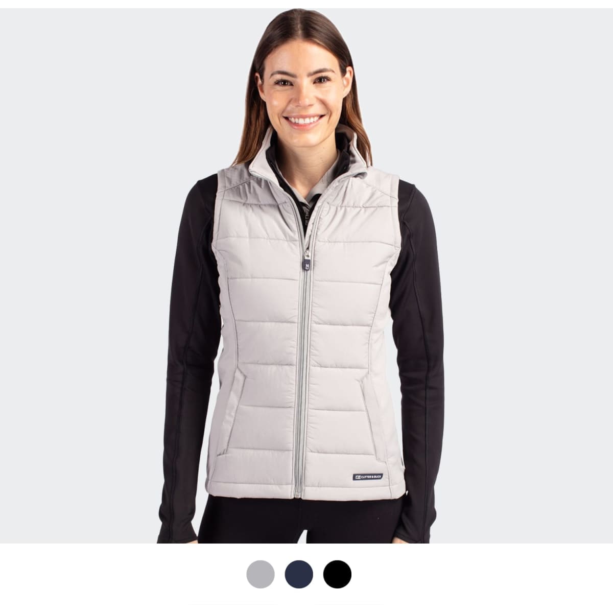 A woman wearing a light grey puffer vest with a zip front. The vest has a logo and is styled with a black top.