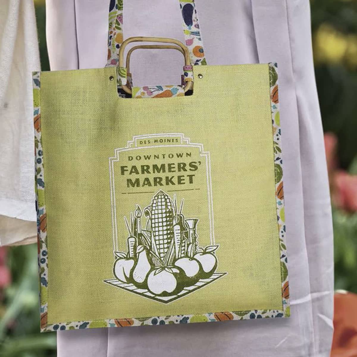 A green jute shopping bag with a handle and a colourful floral design, featuring a farmers' market graphic.