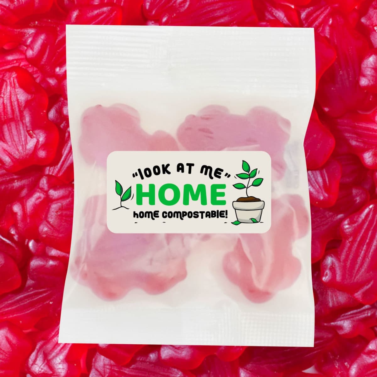 A pack of red gummi frogs, featuring a logo and a label indicating home compostability, against a backdrop of more gummi frogs.