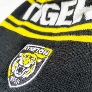 A black and yellow pom pom beanie featuring a logo and bold lettering.