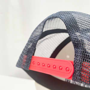 A custom trucker cap featuring a black mesh back and a vibrant red adjustable strap. It has a logo on the front.