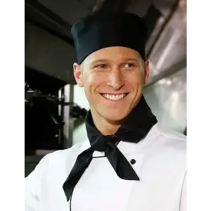 A chef wearing a black scarf and black cap, smiling in a kitchen setting. The scarf complements his white chef's uniform.