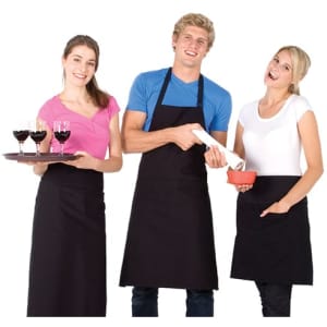Three people wearing black long waist aprons over casual clothing, with one holding a tray of drinks and others holding dishes.