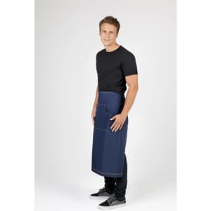 A man wearing a long denim apron with a pocket, standing against a neutral background.