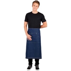 A long waist denim apron in blue with pockets, worn by a smiling man in a black T-shirt and jeans.
