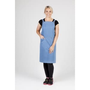 A woman in a denim apron stands confidently, featuring adjustable straps and a pocket, paired with black leggings and pink shoes.