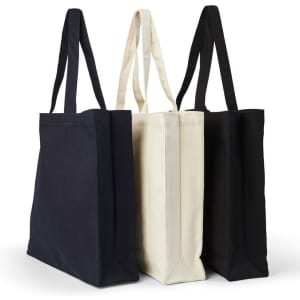A set of three heavy tote bags in black, cream, and navy, each featuring sturdy handles and a logo.
