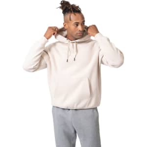 A light beige kangaroo hoodie featuring a front pocket, worn by a model with grey pants. The hoodie has a logo.