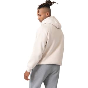 A light beige men's cotton hoodie with a kangaroo pocket, worn with grey sweatpants, featuring a logo on the front.