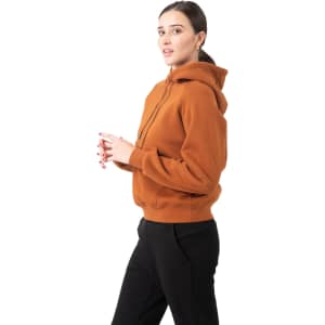 A woman wearing an orange kangaroo pocket hoodie, featuring a hood and a relaxed fit, paired with black pants.